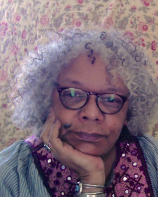 Woman with chin in hand wearing a pink scarf and silver bracelet with gray curly hair