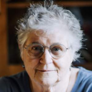 Lois wearing wire rimmed glasses with white hair and blue shirt smiling at the camera