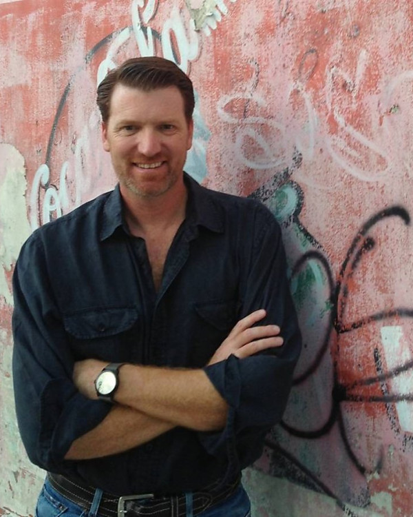 Michael Spurgeon leaning against graffitied wall, smiling.